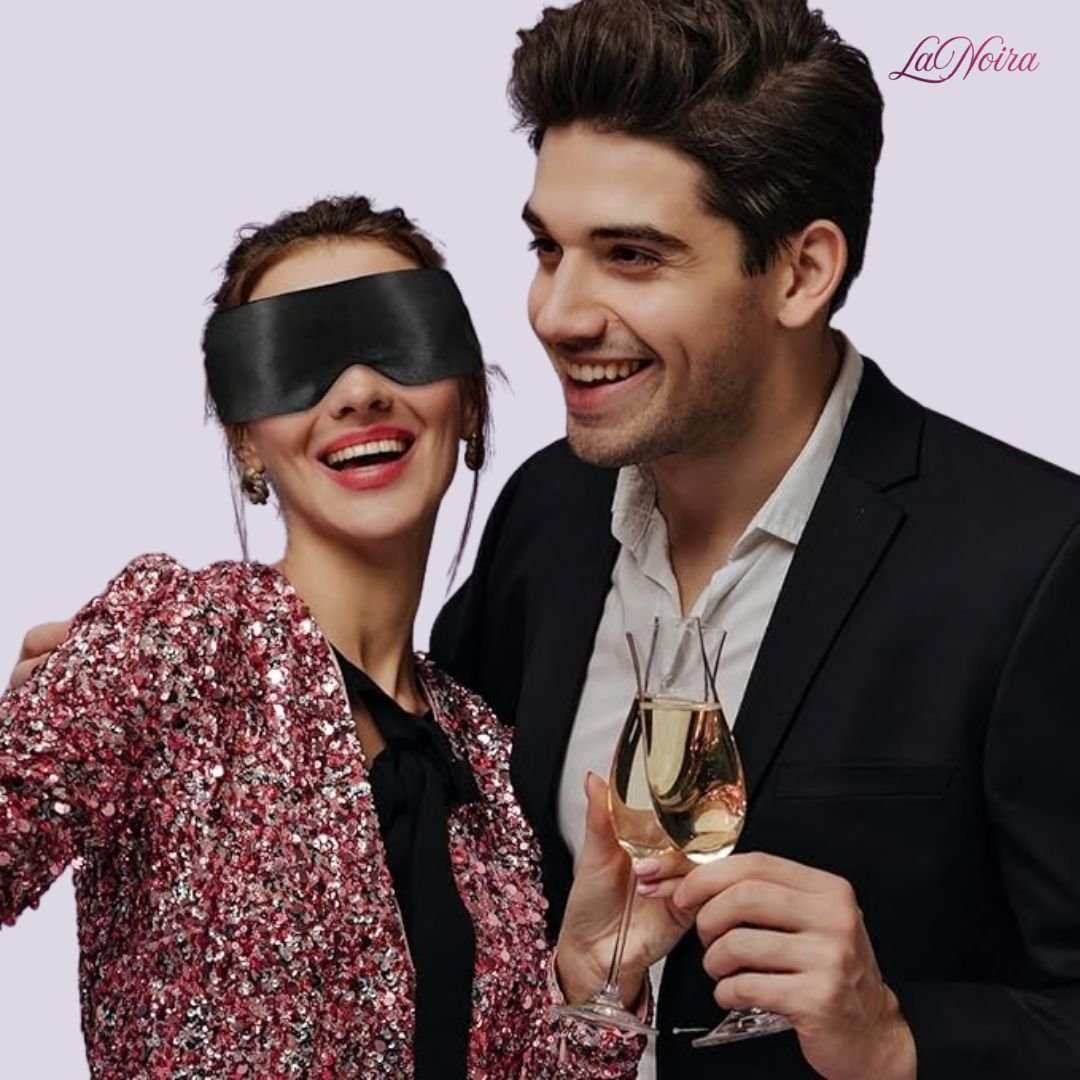 Woman wearing black satin blindfold smiling beside partner holding champagne glasses